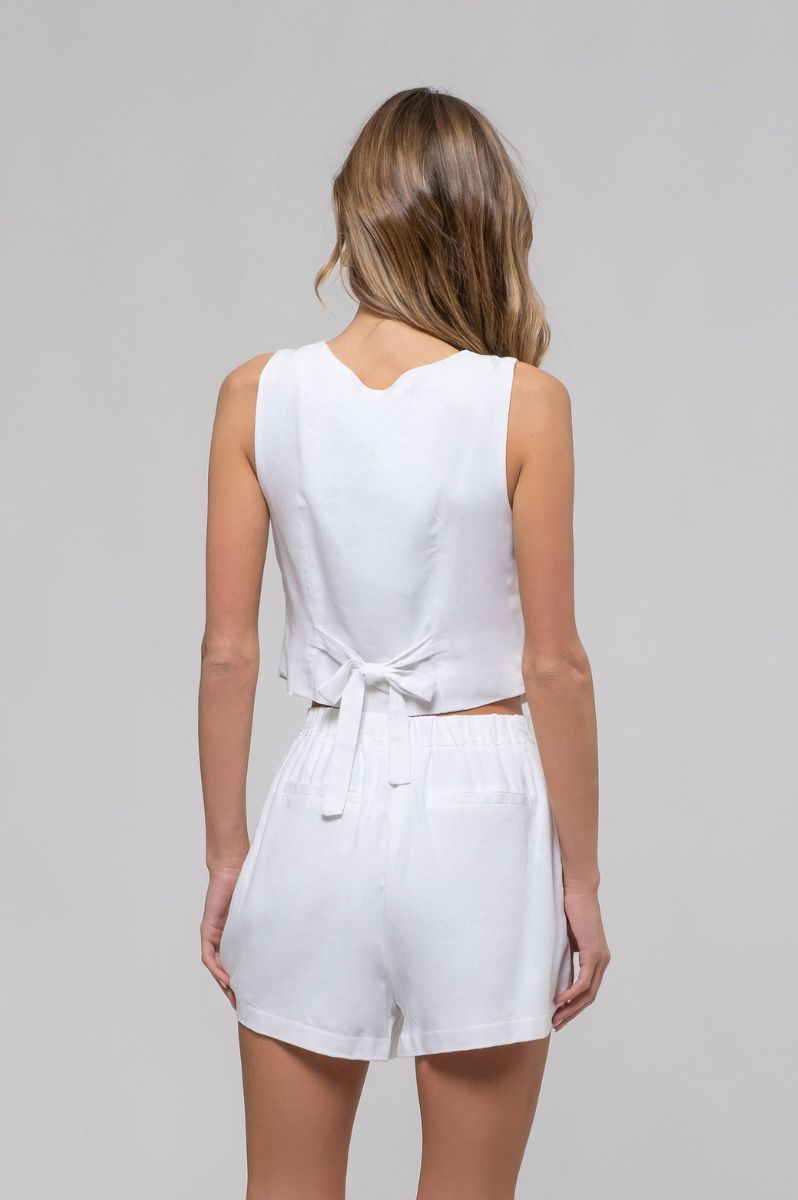 Woman wearing a white sleeveless top and shorts set on a gray background