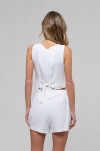 Woman wearing a white sleeveless top and shorts set on a gray background