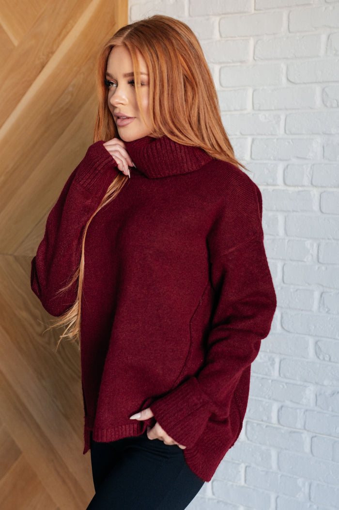 Woman wearing a burgundy sweater against a white brick wall.